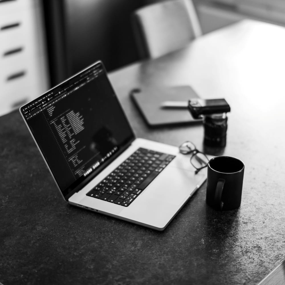 Laptop displaying code and automation tools on a dark workspace desk with a coffee cup, representing AI automation development and software engineering.