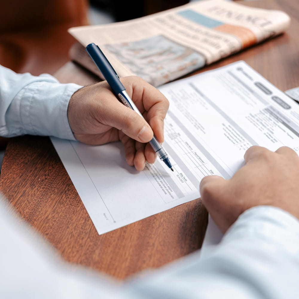 Close-up of a person filling out healthcare billing and medical documentation forms with a pen on a desk.