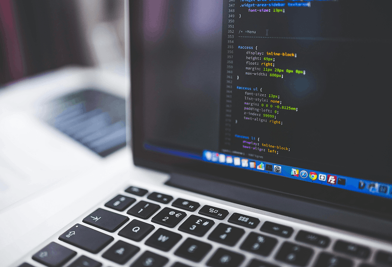 Macro view of a laptop displaying programming code on the screen with a blurred keyboard and workspace background.