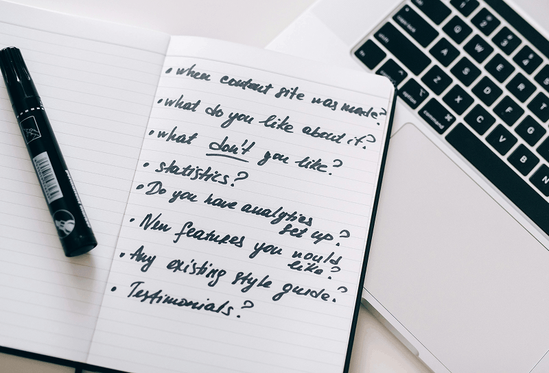 Open notebook with handwritten content writing and website feedback notes placed next to a laptop keyboard and marker pen on a clean workspace desk.