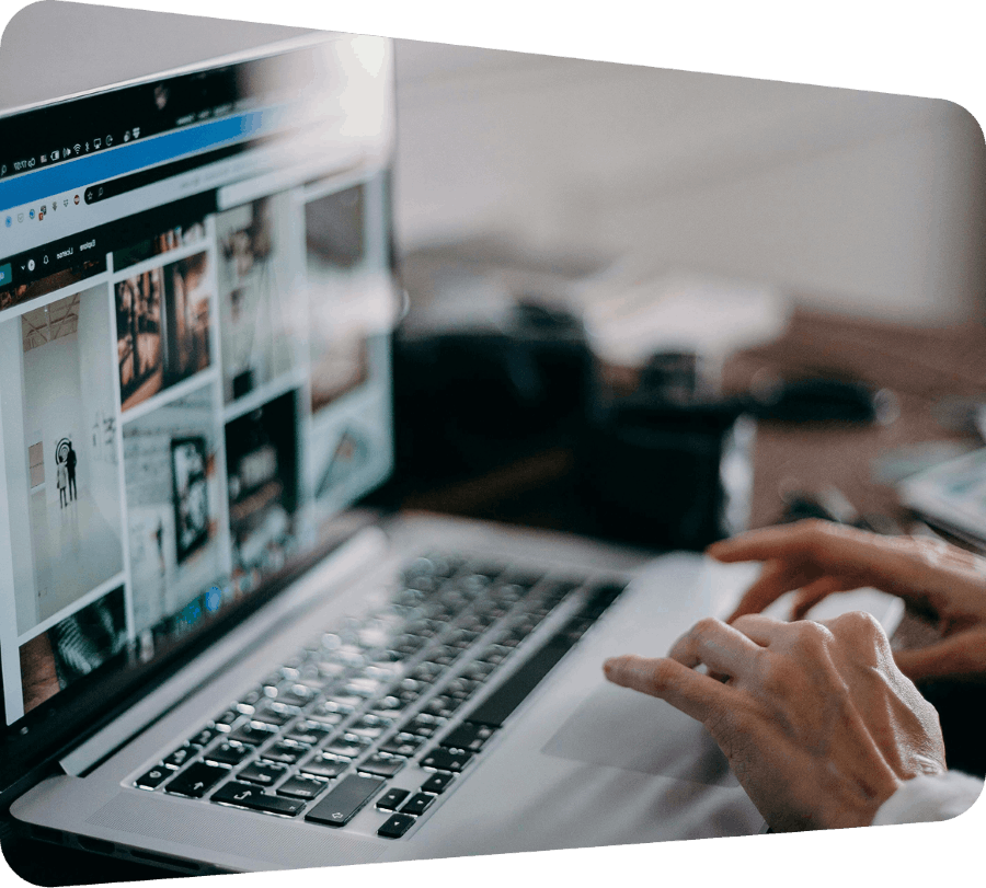 Close-up of a person using a laptop with an image gallery open on the screen in a blurred workspace setting.