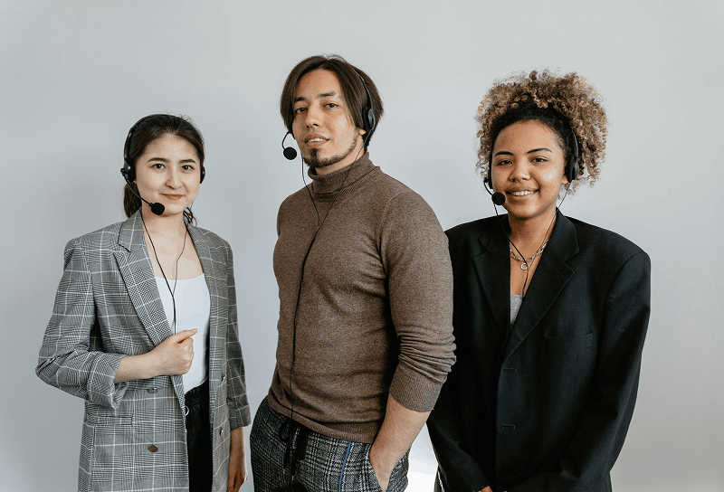 Three customer support professionals wearing headsets and standing together against a neutral background.